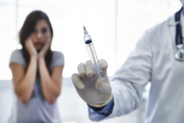 A doctor preparing to give a nervous young woman an injection